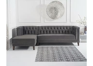 A dark grey sectional sofa featuring a left-hand facing chaise, distinguished by deep button tufting on the backrest and inner arms. The exterior arms and lower front frame are accented with decorative silver nailhead trim. It is upholstered in a soft, plush fabric and stands on short, dark-stained tapered wooden legs. The design combines classic Chesterfield elements with a contemporary sectional form. — 3D model