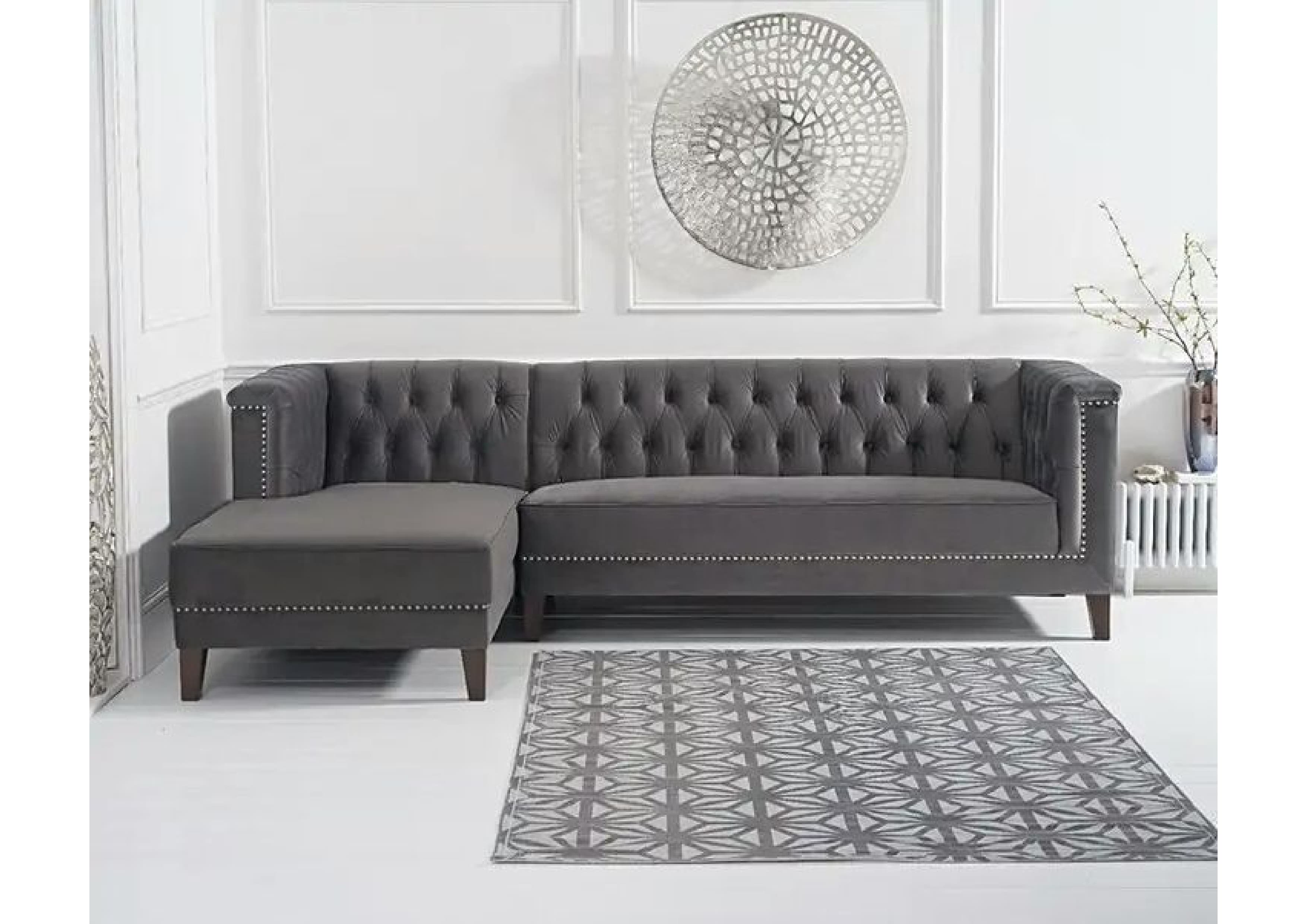 A dark grey sectional sofa featuring a left-hand facing chaise, distinguished by deep button tufting on the backrest and inner arms. The exterior arms and lower front frame are accented with decorative silver nailhead trim. It is upholstered in a soft, plush fabric and stands on short, dark-stained tapered wooden legs. The design combines classic Chesterfield elements with a contemporary sectional form. — 3D model