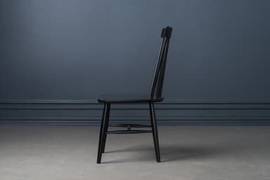 A classic black lacquered Windsor-style dining chair, featuring a tall spindle backrest and a solid wood saddle-shaped seat. The chair stands on four splayed and tapered legs, reinforced by H-stretchers, offering a timeless and sturdy design. — 3D model