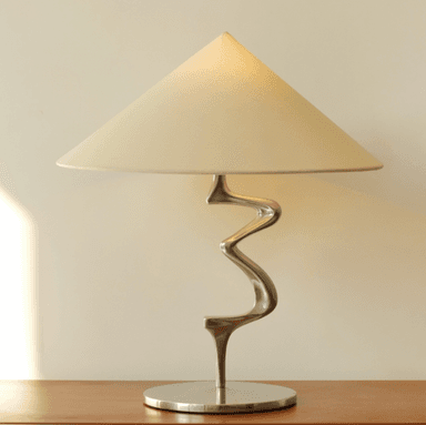 A modern table lamp featuring a distinctive serpentine metal stem, a circular base, and a conical fabric shade. The design emphasizes sculptural form and a polished finish. — 3D model