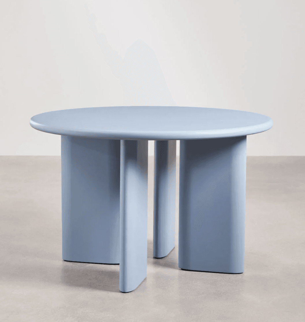 A contemporary round coffee table featuring a light blue, monochromatic finish and a distinctive base composed of three broad, segmented pedestal-like legs. The table top is perfectly circular with rounded edges, and the legs are thick, flat, and slightly curved, providing a sturdy and minimalist aesthetic. The overall design suggests modern, sculptural furniture. — 3D model