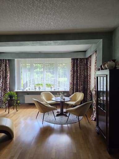 A contemporary dining set featuring a small round wooden table and four matching upholstered chairs, positioned on a decorative circular rug. The chairs have light yellow fabric upholstery and slender, splayed black metal legs, complementing the dark wooden tabletop with similar leg design. — 3D model