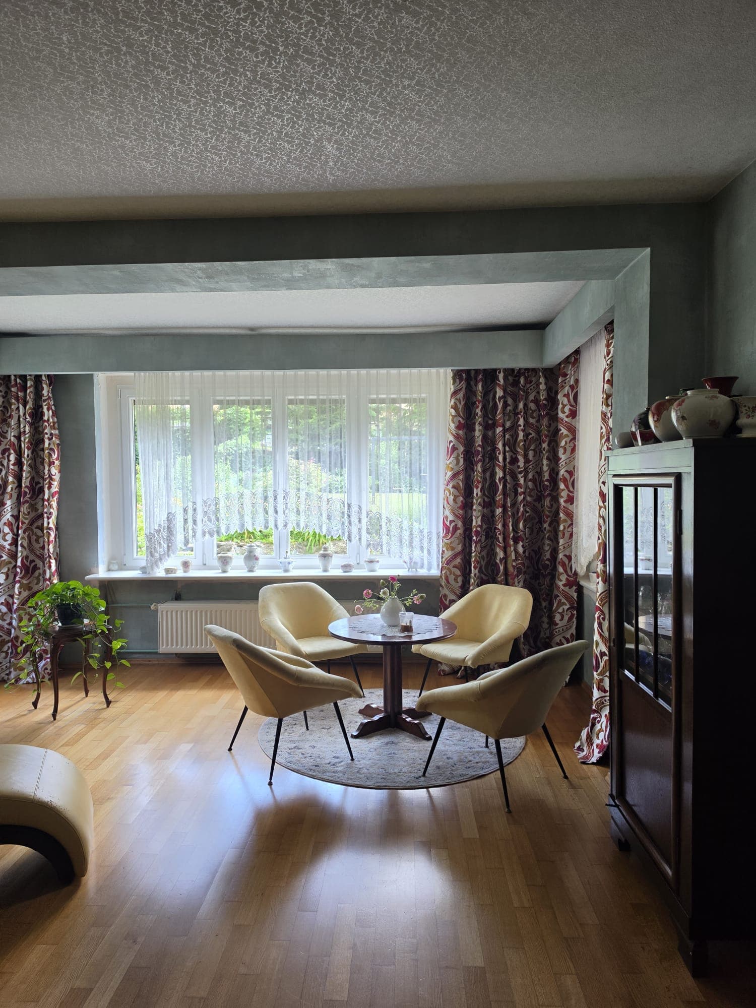 A contemporary dining set featuring a small round wooden table and four matching upholstered chairs, positioned on a decorative circular rug. The chairs have light yellow fabric upholstery and slender, splayed black metal legs, complementing the dark wooden tabletop with similar leg design. — 3D model