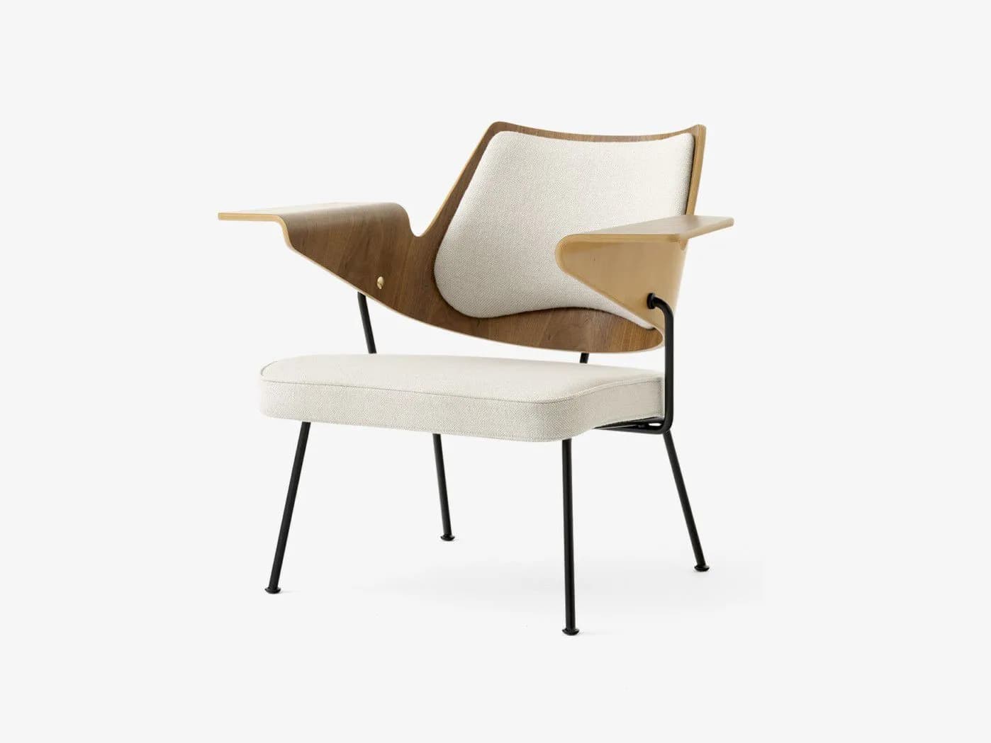 A modern, sculptural lounge chair featuring a combination of bent plywood, light-colored upholstery, and a black metal frame. The backrest and armrests are formed from curved plywood, with a distinctive, integrated writing tablet made of a contrasting lighter wood or laminate on the right arm. The seat and an oval-shaped back cushion are upholstered in a textured, off-white fabric. The chair is supported by four slender, splayed black metal legs. — 3D model