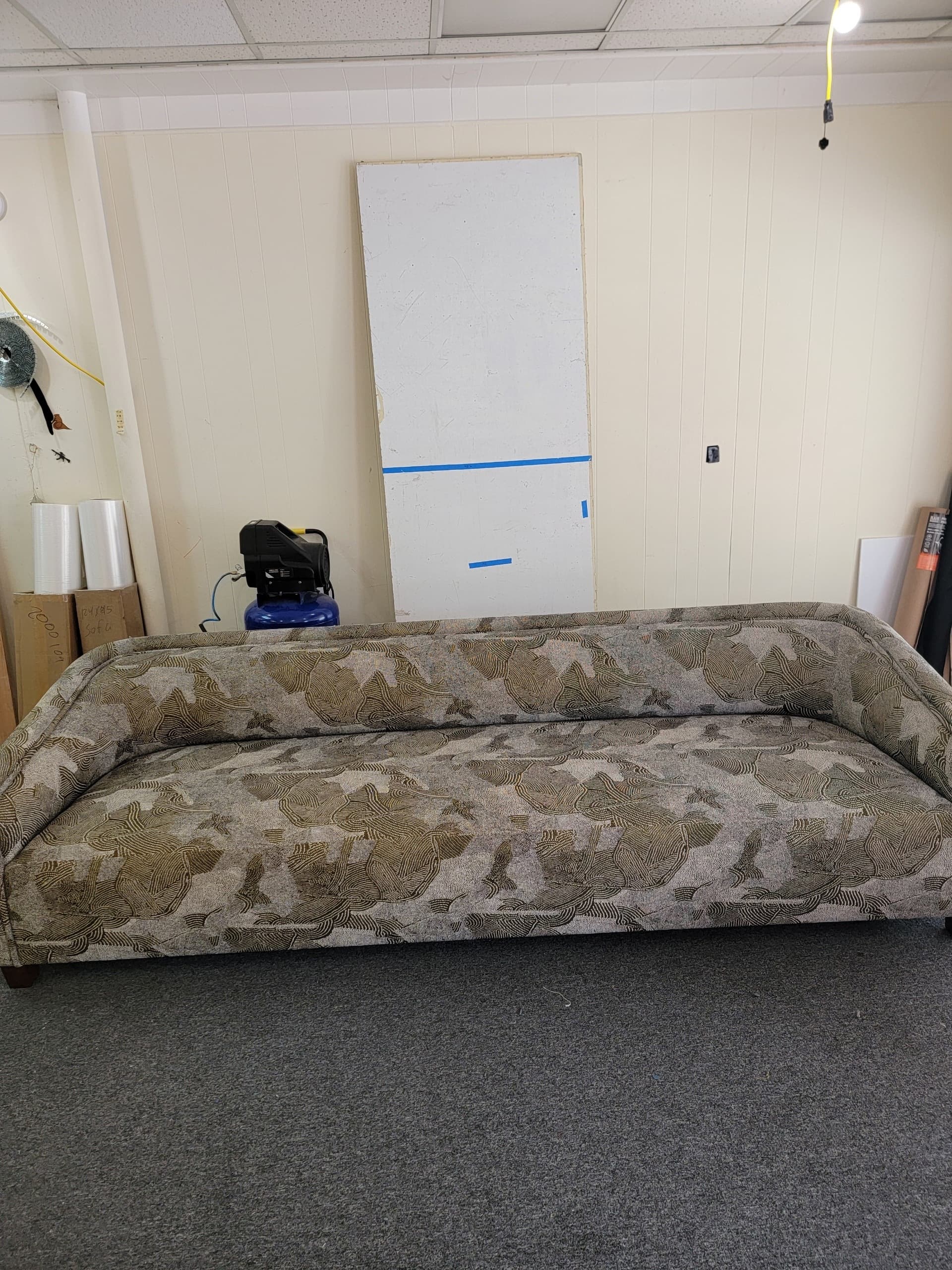 A contemporary three-seater sofa featuring a distinctive abstract pattern upholstered fabric. The sofa has a continuous backrest and gently curved arms that flow seamlessly into the back. It is supported by short, recessed dark wooden feet, giving it a low-profile stance. The fabric pattern consists of organic, wavy lines and shapes in varying shades of beige, brown, and olive green. — 3D model