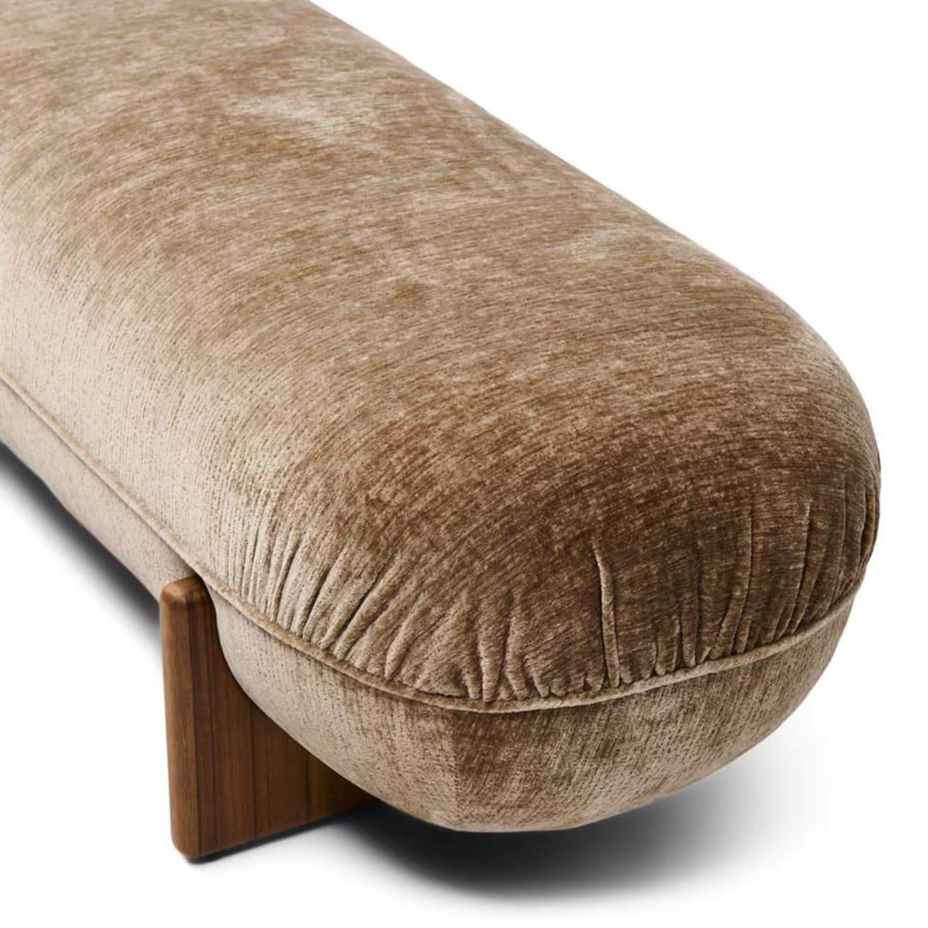 A low-profile, elongated bench with a rounded, upholstered form and solid wood legs. The upholstery features a textured, velvet-like fabric in a neutral tone, exhibiting subtle creasing that follows the rounded shape. The legs are triangular in cross-section and appear to be made of a dark wood with a visible grain. — 3D model