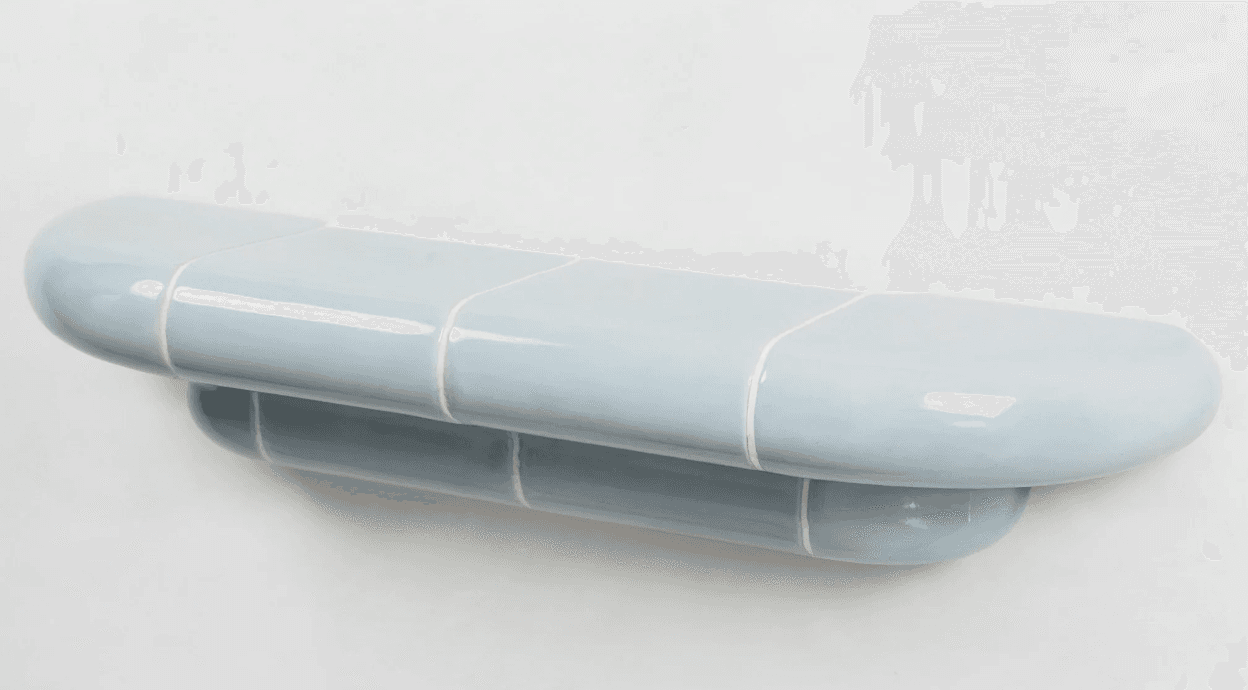 A pill-shaped, wall-mounted shelf constructed from glossy light blue ceramic or tiled elements. The design features a larger rounded top surface and a slightly smaller, similarly shaped element beneath it, both exhibiting visible grout lines. The overall aesthetic is modern and minimalist with soft, rounded edges. — 3D model