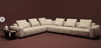 An L-shaped modular sectional sofa, upholstered in a light beige fabric, featuring a minimalist design with a low-profile, recessed dark plinth base. The sofa is composed of multiple individual units arranged in a corner configuration, providing extensive seating. It includes numerous loose back cushions and throw pillows, enhancing comfort and aesthetic appeal. The overall appearance is modern and clean-lined. — 3D model