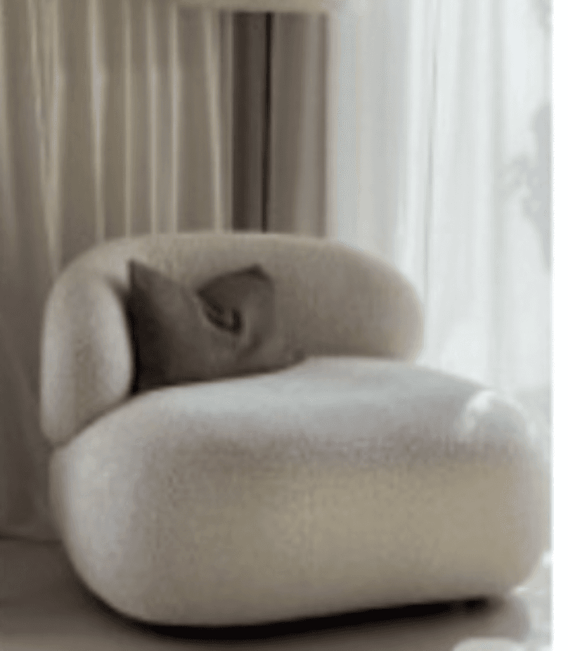 A single-seater armchair with a rounded, organic silhouette. The upholstery appears to be a textured boucle fabric, providing a soft and inviting aesthetic. It features a low profile and a generously proportioned seat and backrest. A rectangular throw pillow in a muted green hue is placed against the backrest. — 3D model