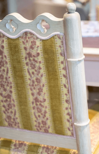 A side chair with a light-colored, possibly painted wooden frame. The frame features faux bamboo turnings on the legs and structural elements, with decorative carvings at the top of the backrest. The seat and backrest are upholstered with fabric that has a pattern of alternating wide golden yellow stripes and narrower stripes with a floral or damask-like motif in a darker pinkish-red and yellow. The upholstery appears to be velvet or a similar textured fabric. — 3D model