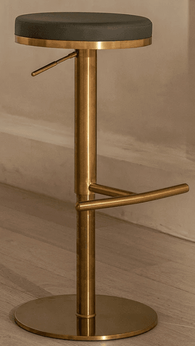 A modern adjustable bar stool featuring a round, dark grey upholstered seat and a polished brass finish on its metal components. The stool has a central cylindrical column for height adjustment, a curved circular footrest, and a sturdy flat disc base for stability. Its sleek design and material combination suggest a contemporary aesthetic. — 3D model