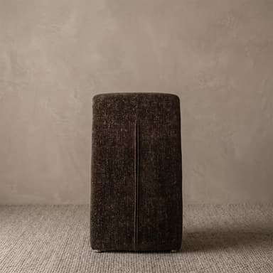 An armless chair featuring a unique, continuous sculptural form, fully upholstered in a dark brown, textured fabric. The seat flows seamlessly into the base, eliminating traditional legs, while a rounded, integrated back cushion provides support. — 3D model
