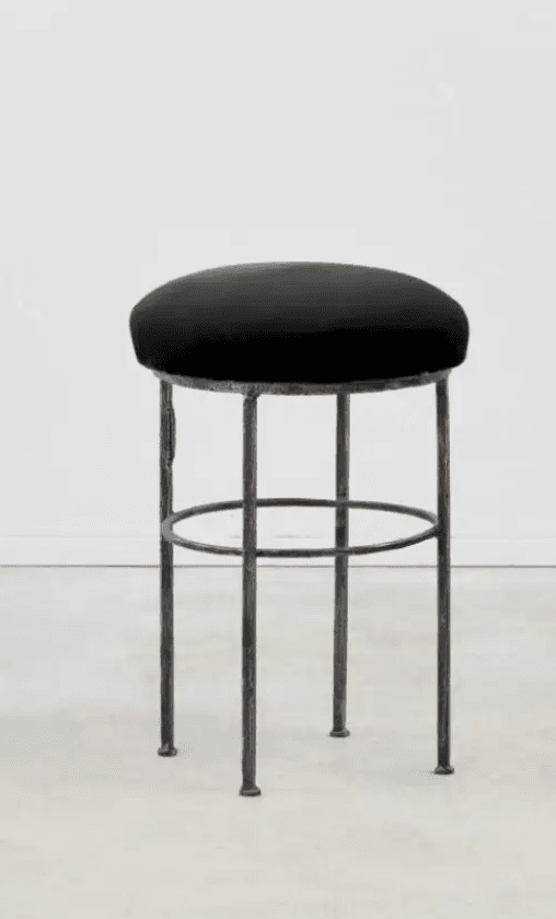 A black bar stool with a round, upholstered seat and a base constructed from four slender, dark metal legs. The legs are connected by a circular metal ring positioned about halfway down, providing structural support and a footrest. — 3D model