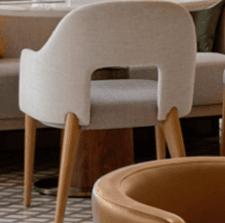 A contemporary upholstered armchair featuring a curved backrest that seamlessly transitions into integrated armrests. The chair is covered in a light beige or oatmeal-colored fabric and stands on four slender, tapered light-toned wooden legs. A distinctive cutout is present at the lower back of the chair, enhancing its modern aesthetic and offering a subtle visual lightness. — 3D model