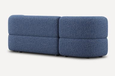 A low-profile, modular sofa with rounded edges and a textured fabric upholstery. The sofa appears to be constructed from densely packed foam or similar cushioning material. It features a distinct layered design for both the seat and backrest. Small, dark cylindrical legs support the base. — 3D model