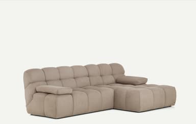 A light beige, modular sectional sofa featuring a chaise lounge component on the right side. The entire sofa is upholstered in a ribbed corduroy fabric, giving it a plush, textured appearance. It consists of deep, blocky cushions for both the seat and backrest, arranged in a low-profile, contemporary style. The armrests are similarly upholstered and integrated, providing a soft, rounded look. — 3D model