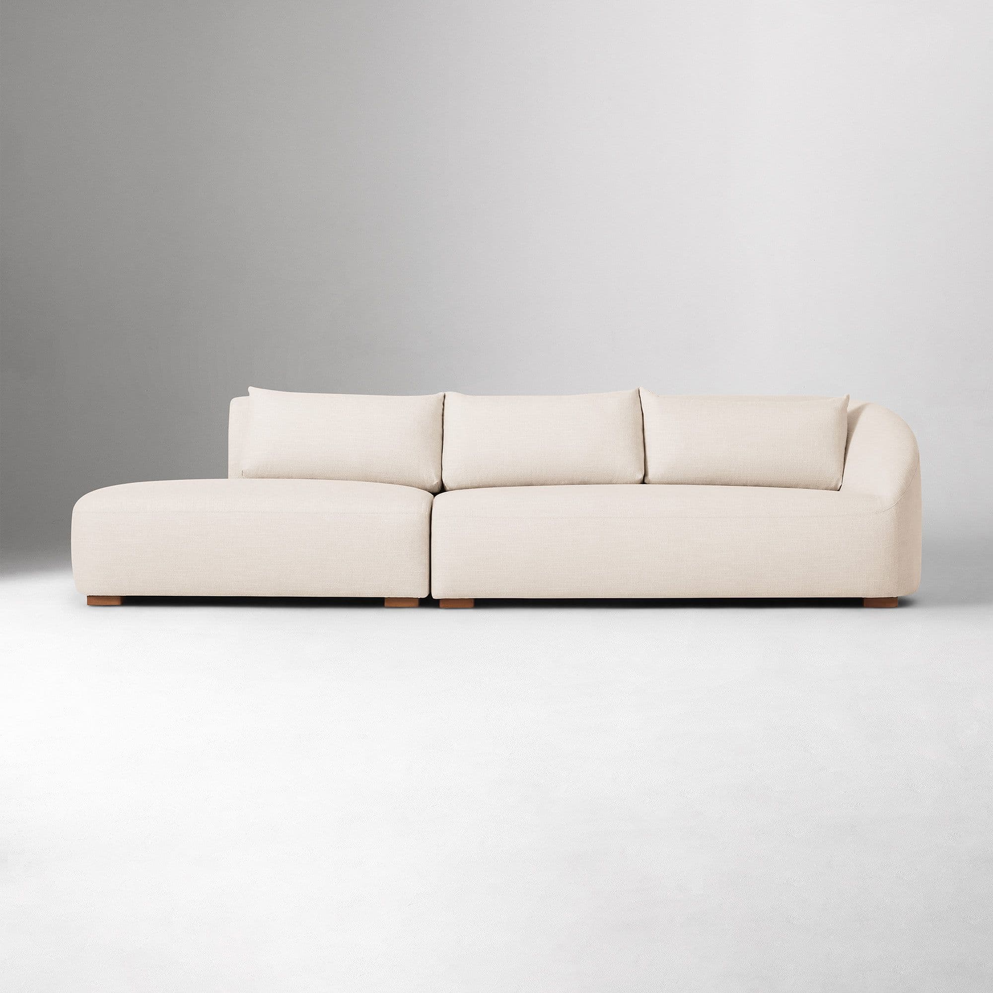 A sectional sofa with a chaise lounge. The sofa has a low profile and is upholstered in a textured fabric. It features plush back cushions and a rounded armrest on the chaise end. The sofa is supported by small, dark wooden block feet. — 3D model
