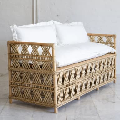 A rattan daybed with a woven geometric pattern on the sides and back. It features thin, cylindrical legs and is topped with two white pillows and a white mattress or cushion. — 3D model