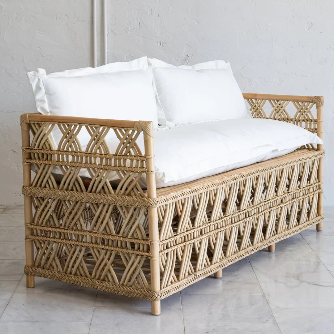 A rattan daybed with a woven geometric pattern on the sides and back. It features thin, cylindrical legs and is topped with two white pillows and a white mattress or cushion. — 3D model