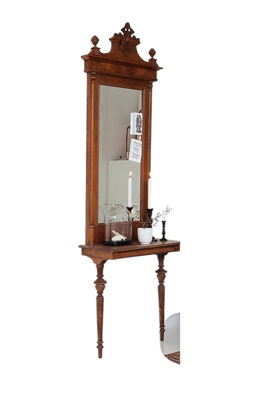 A tall, ornate wooden console table integrated with an upright mirror. The piece features elaborate carvings, finials, and turned legs, characteristic of Victorian-era design. The dark wood has a visible grain and appears to be solid hardwood. The mirror is framed by the carved wood, and a small console surface is positioned below it, supported by two turned front legs. The surface shows some signs of age and wear. — 3D model