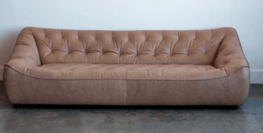 A contemporary sofa featuring an asymmetrical backrest and deep button tufting, upholstered in beige leather with a low-profile silhouette and recessed feet. — 3D model