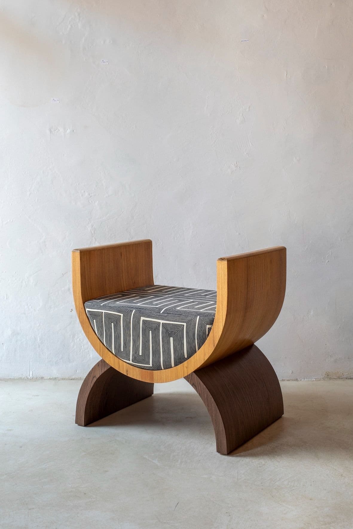 A modern stool with a curved wooden frame and a upholstered seat. The frame consists of two C-shaped wooden elements that support a central upholstered cushion. The backrest is formed by two upright, curved wooden pieces that extend upwards from the sides of the seat. — 3D model