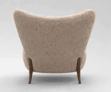 An armchair featuring a rounded, plush silhouette upholstered in a cream or beige bouclé fabric. It has visible, smoothly curved dark wooden armrests that extend downwards to form the front legs, and splayed wooden back legs. The backrest is slightly flared, providing a comfortable seating experience. — 3D model