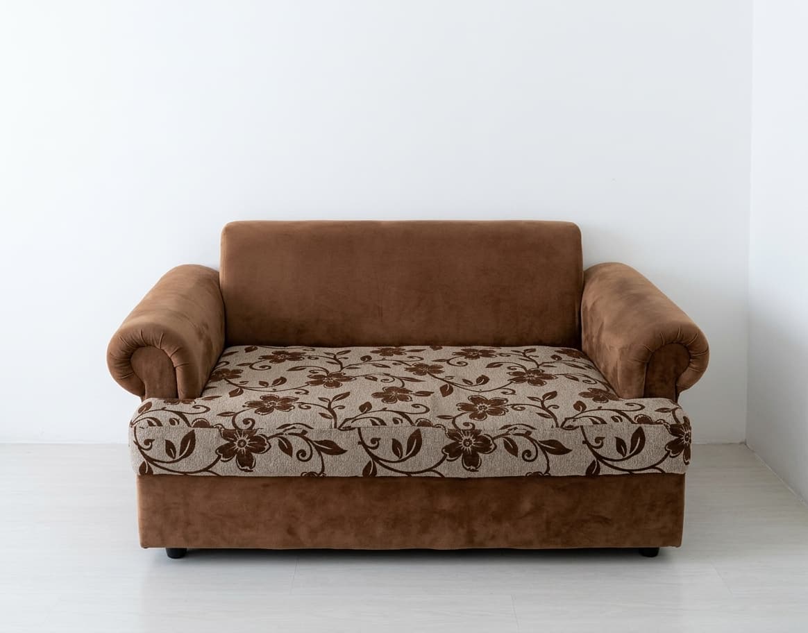 A compact two-seater loveseat featuring rolled armrests and a high backrest. The frame and armrests are upholstered in a solid light brown velvet-like fabric, while the single seat cushion is adorned with a beige background and a repeating pattern of dark brown floral motifs. The loveseat rests on discreet dark feet. — 3D model