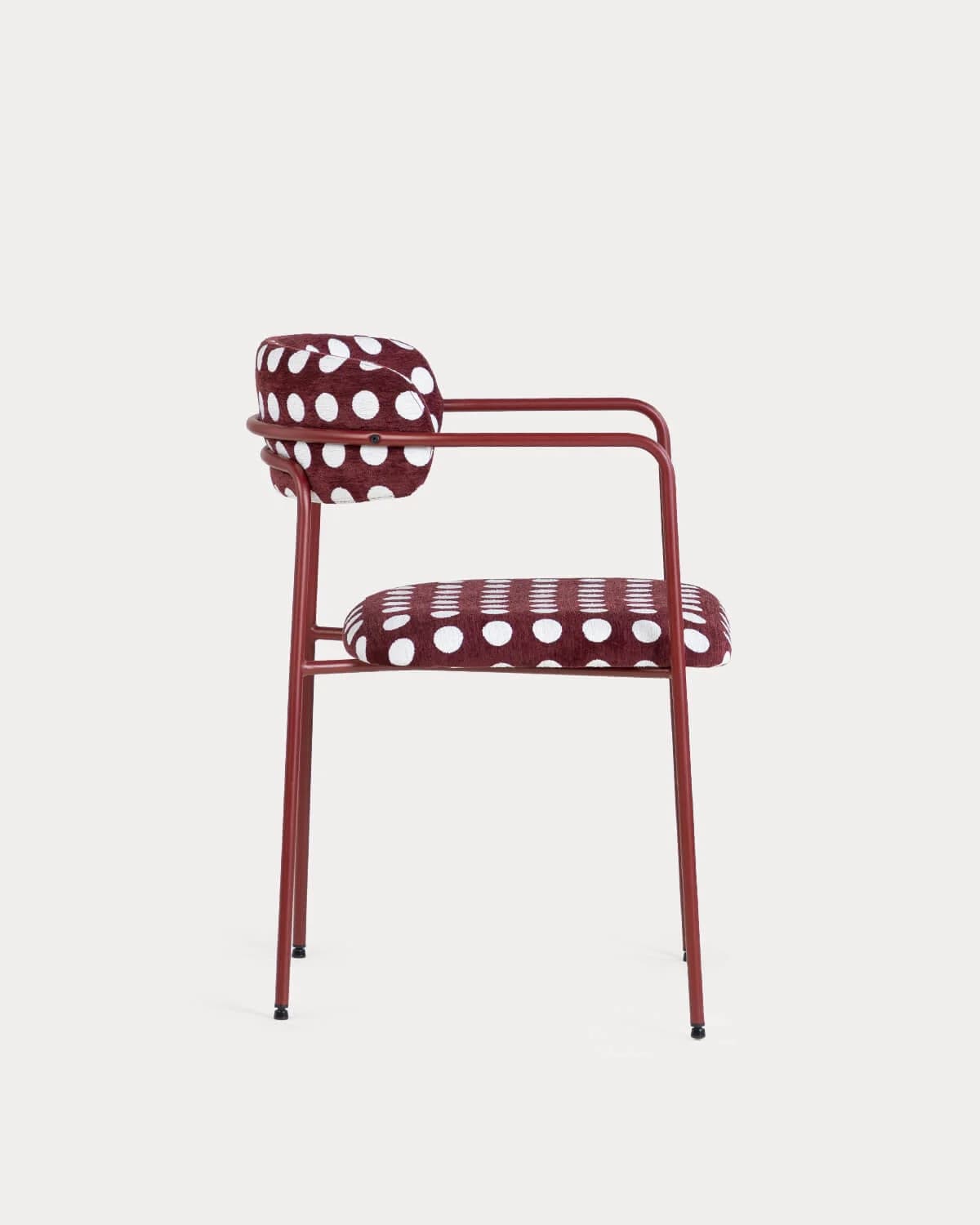 A contemporary armchair featuring a tubular metal frame finished in a matte red or burgundy hue. The seat and a separate backrest cushion are upholstered in a contrasting burgundy fabric with a white polka-dot pattern. The armrests are integrated into the frame structure, extending from the front legs and curving upwards to meet the backrest support. — 3D model