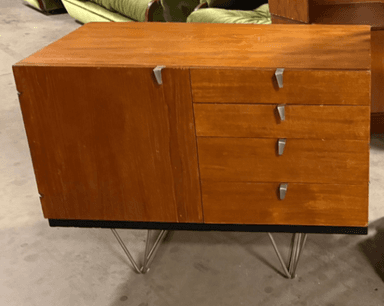 A modern cabinet with a wood-grain finish, featuring a single door on the left and four drawers stacked vertically on the right. It is elevated by thin, angular metal legs, giving it a mid-century modern aesthetic. The handles are silver-toned and minimalist. — 3D model