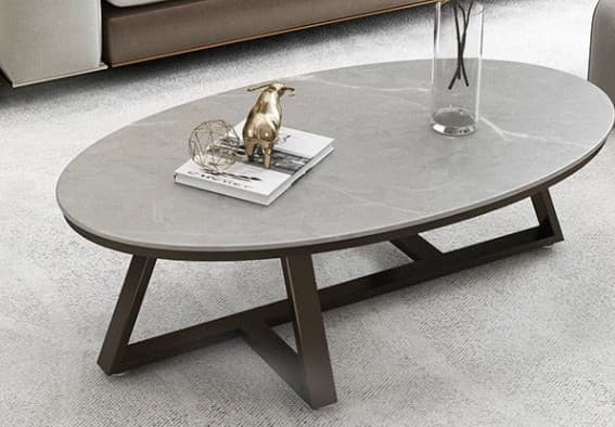 An oval coffee table featuring a light grey top with subtle white veining, resembling marble, supported by a dark brown or bronze-finished metal base with angled, geometric legs. — 3D model