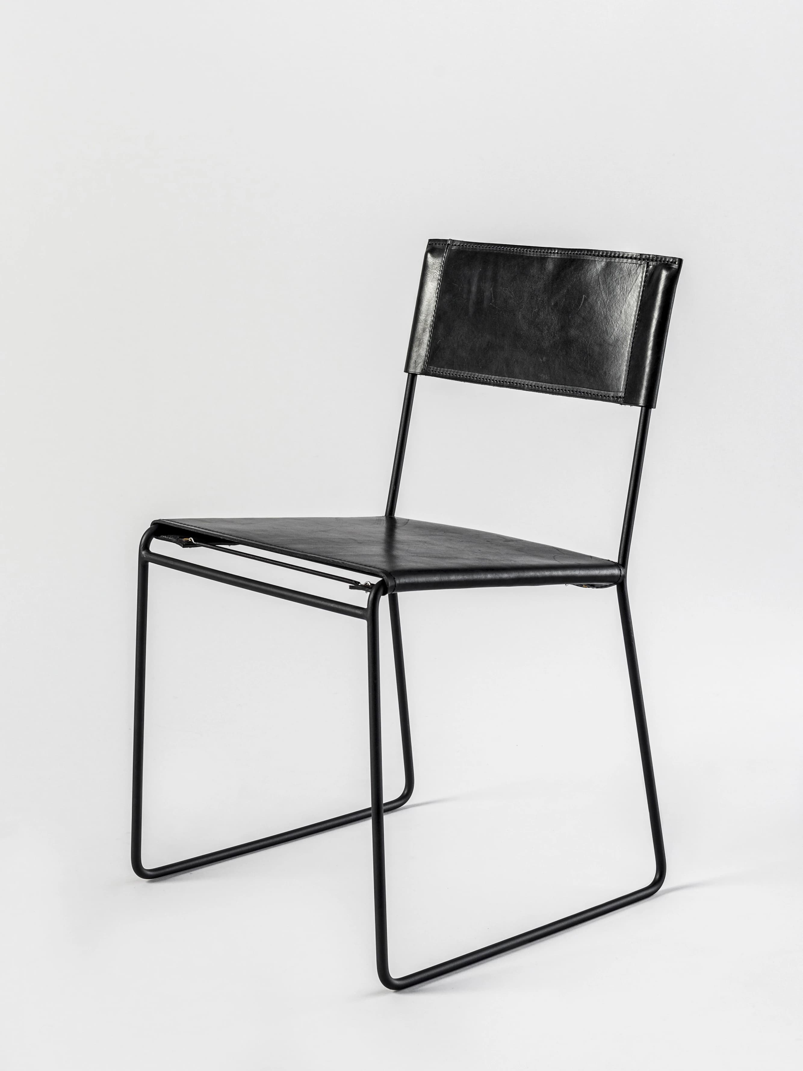 A contemporary armless chair featuring a minimalist design with a black metal sled frame and black leather upholstery for the seat and back. — 3D model