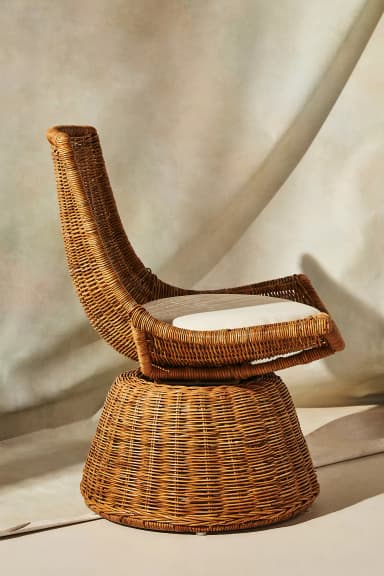 A contemporary lounge chair crafted from natural woven rattan, featuring a wide, curving backrest and a conical base that allows for 360-degree swivel movement. It includes a round, off-white seat cushion for added comfort. — 3D model