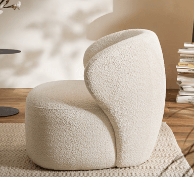 A contemporary lounge chair upholstered in a textured, cream-colored bouclé fabric. The chair features a distinctive, organic silhouette with a rounded back that seamlessly transitions into the armrests and seat, creating a unified and inviting form. Its low profile and plush cushioning suggest comfort and relaxation, making it a statement piece for modern interiors. — 3D model
