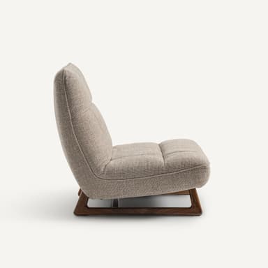 A modern armchair with a low profile and a sloped backrest. The armchair features upholstered seating and back cushions with subtle tufting. It is supported by a minimalist wooden base with angled legs. — 3D model