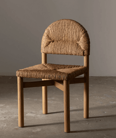 An armless side chair featuring a light-toned wooden frame and tightly woven natural rush or seagrass for both the seat and the arched backrest. The design is simple and organic, with straight, round tapered legs and a minimalistic cross-brace structure under the seat for stability. The woven elements provide texture and a natural aesthetic. — 3D model