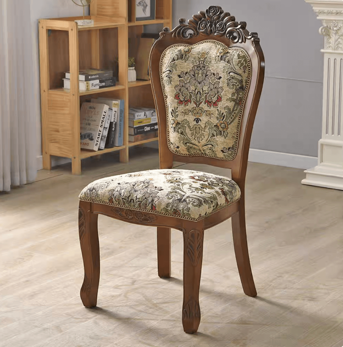 An ornate traditional dining side chair featuring a dark brown carved wood frame and upholstered seat and back. The chair exhibits classical design elements, including an elaborately carved crest rail and cabriole front legs with detailed acanthus leaf carvings. Both the seat and the backrest are upholstered in a patterned fabric, likely a jacquard or tapestry, featuring a multi-color floral motif on a light background, finished with decorative nailhead trim along the edges. — 3D model