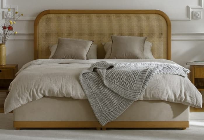 A modern platform bed featuring a light natural wood frame, a rounded headboard with cane webbing, and an upholstered bed base in a light beige fabric. The bed is shown with light-colored bedding and a grey knitted throw. — 3D model