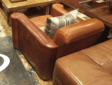 A brown leather armchair with a plaid cushion placed on the seat. The armchair has rolled arms and a slightly distressed leather finish. The backrest is visible, as is part of the seat and the front of the rolled arms. — 3D model