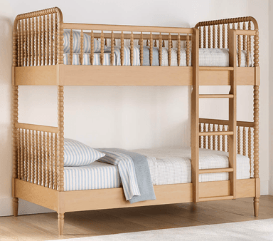 A light-colored wooden bunk bed featuring a classic design with turned spool spindles on both the upper and lower bunks. The bed includes a built-in ladder for access to the top bunk and is outfitted with light-colored, patterned bedding. — 3D model