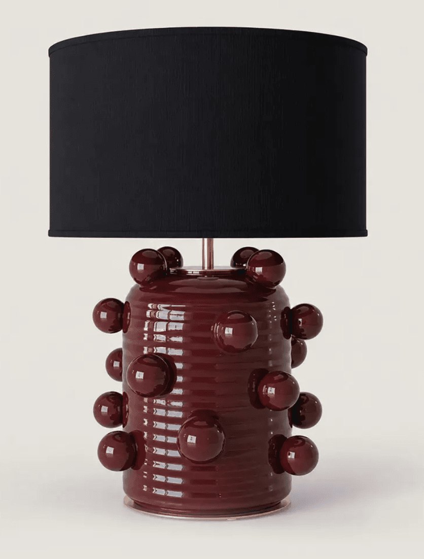 A decorative table lamp featuring a cylindrical ceramic base with a ribbed texture and numerous applied glossy spherical accents. The base is finished in a deep burgundy glaze and topped with a simple, cylindrical black fabric drum shade, supported by a small brass-toned neck. — 3D model