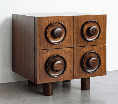 A compact, rectangular wooden cabinet featuring a dark stained finish and distinctive sculptural circular handles on each of its four front panels. The cabinet stands on four robust cylindrical legs, and its top surface appears to be a lighter, contrasting material. The design is notably geometric and tactile. — 3D model