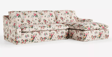 A cream-colored sofa upholstered in a floral fabric with a pattern of roses, peonies, and other flowers in shades of pink, yellow, green, and red. The sofa features a low profile with a slightly sloped armrest. The upholstery covers the entire structure, including the base, cushions, and back. — 3D model