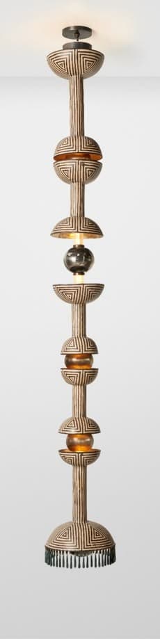 A very tall, multi-tiered pendant light featuring an elongated, segmented design. The main body is decorated with a black and off-white geometric pattern, possibly tribal or Art Deco inspired. It incorporates several spherical and semi-spherical glass elements, some in a warm amber tone, and a darker, possibly smoked glass sphere in the middle. The fixture hangs from a dark ceiling rose and ends with a fringe-like detail at the bottom. — 3D model