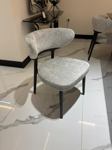 A modern upholstered chair with a curved backrest and a seat. The chair has four tapered legs and appears to be made of wood or metal with a dark finish. The upholstery is a textured fabric in a neutral tone. — 3D model