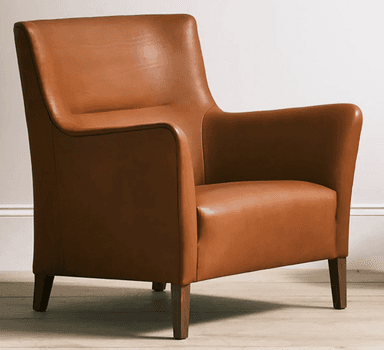 A contemporary armchair upholstered in cognac-colored leather, featuring a broad seat, low-profile rolled armrests, and a gently angled backrest. The chair is supported by four tapered wooden legs, visible beneath its substantial body. Visible stitching defines the edges and seams of the upholstery, contributing to its tailored appearance. — 3D model