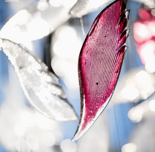 Close-up image of translucent art glass elements, primarily in magenta and clear tones, which are components of a larger lighting fixture. The elements feature an organic, leaf-like shape with a distinct ribbed texture. — 3D model