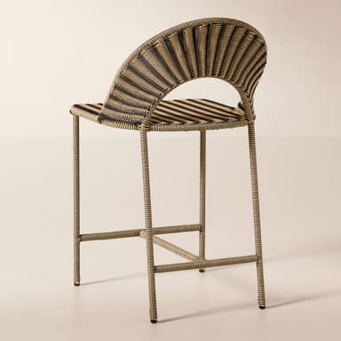 A close-up image of a contemporary accent chair constructed from two-tone synthetic rattan. The chair features a tightly woven pattern in alternating bands of black and light beige, creating a striped effect. It has a curved backrest and integrated armrests, suggesting a comfortable, ergonomic form. The legs, visible at the bottom, also appear to be wrapped in the same woven material, indicating a cohesive design. The texture is smooth and uniform, characteristic of synthetic materials. — 3D model