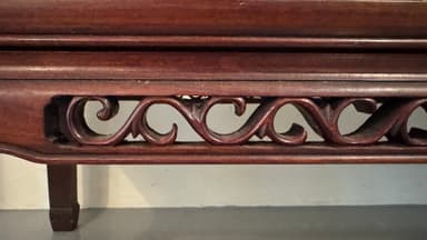 A dark brown, rectangular wall shelf with decorative carved scrolling patterns on its front apron. The shelf has a flat top surface and features a stepped molding detail along the top edge of the front apron. The sides have a slight taper and are also finished in the same dark brown hue. The overall construction appears solid, suggesting a wood material. — 3D model