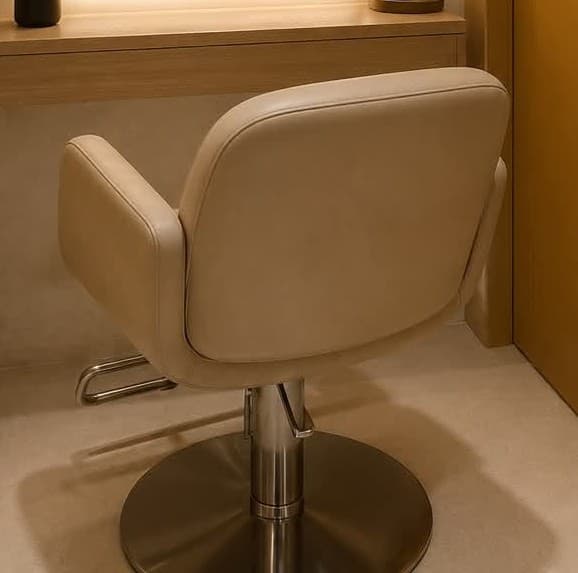 A modern swivel armchair featuring a fully upholstered seat and back in a neutral beige or tan tone, resting on a polished or brushed metal pedestal base. The chair's design is characterized by its smooth, rounded lines and absence of sharp angles, offering a contemporary aesthetic. The seat is cushioned for comfort, and the integrated arms flow seamlessly from the backrest. The circular disc base provides stability and the swiveling functionality. — 3D model